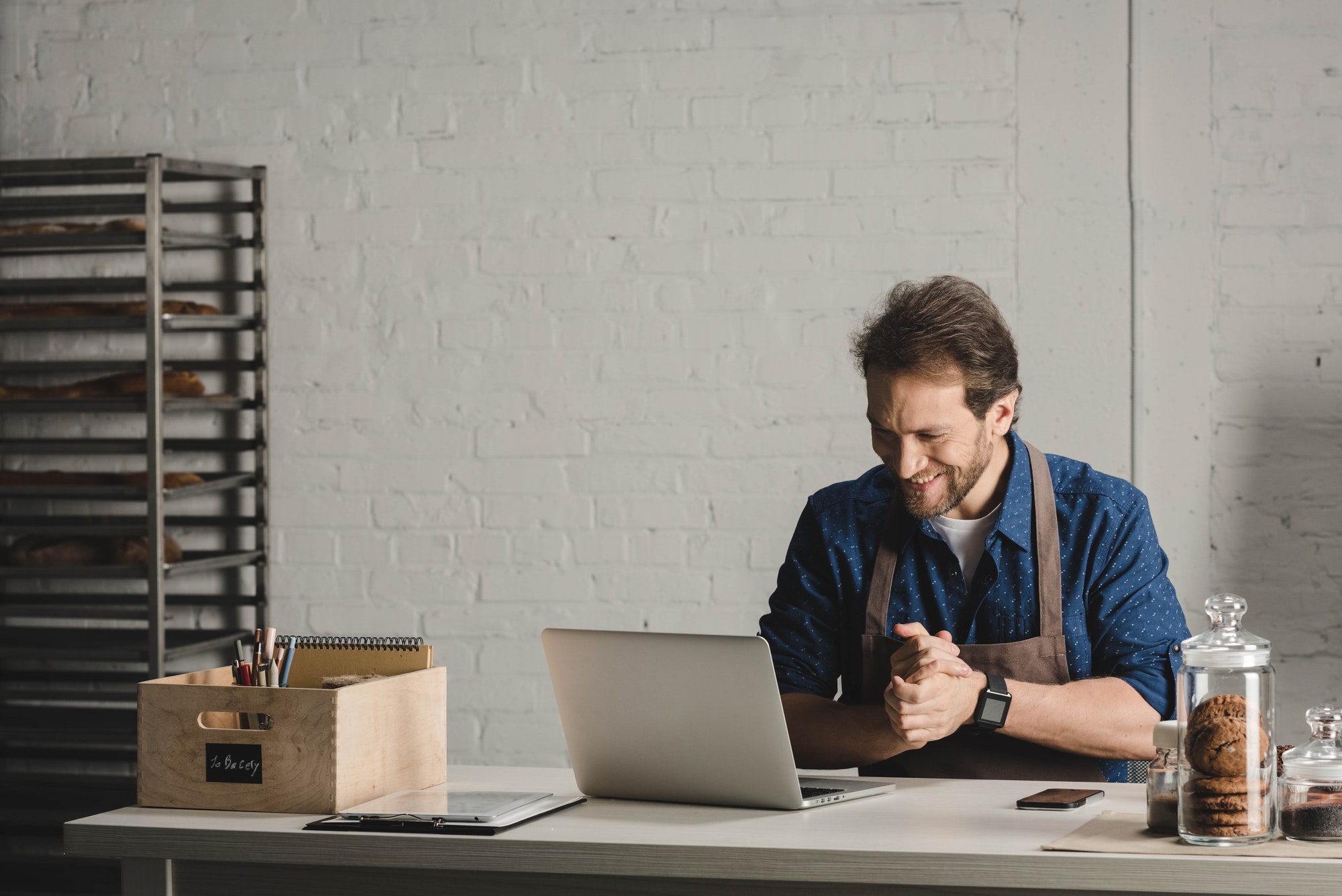 Smiling man in apron working with laptop at the bakery